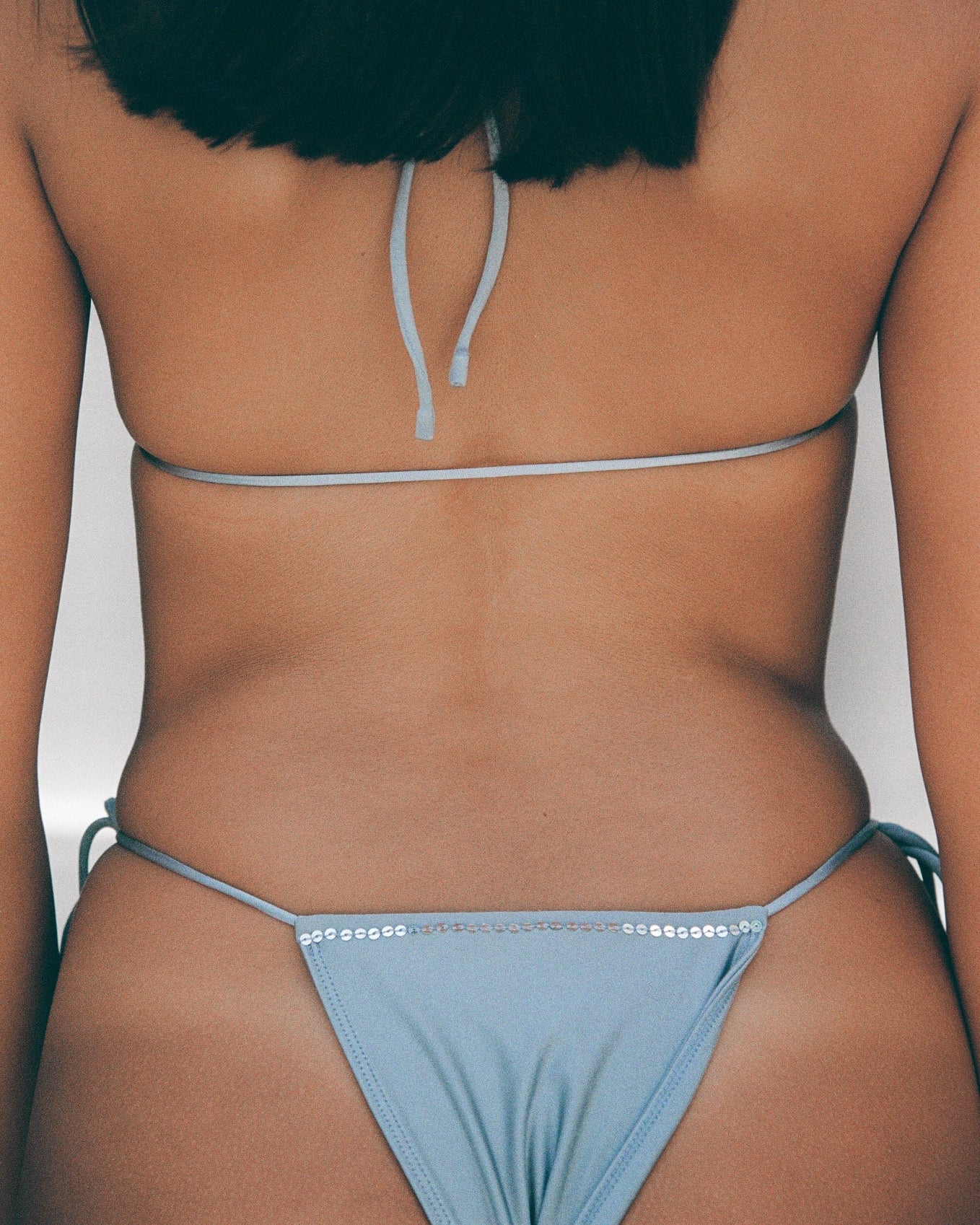 woman wearing a light blue sequin bikini against a neutral background
