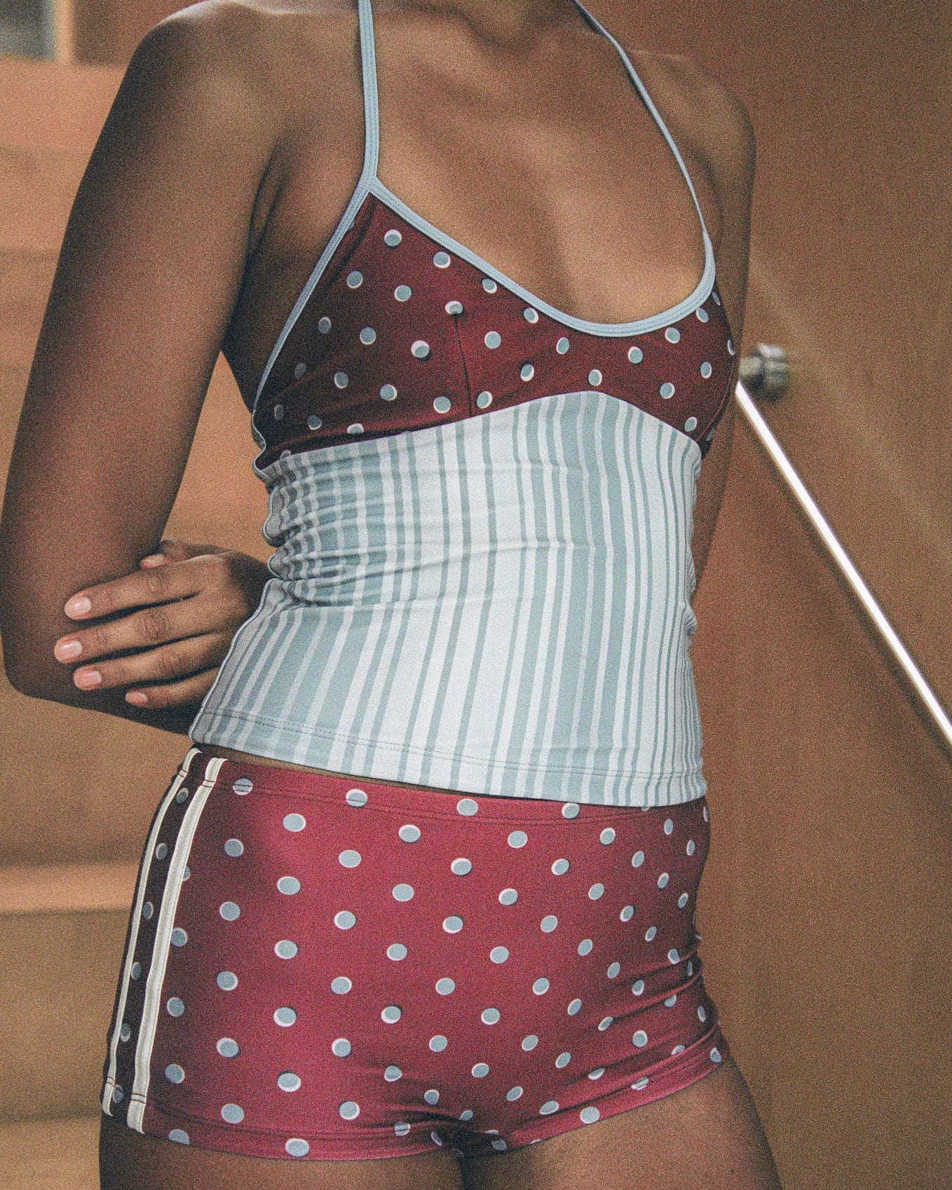 Woman wearing a polka dot and stripe swimsuit with a neutral background.