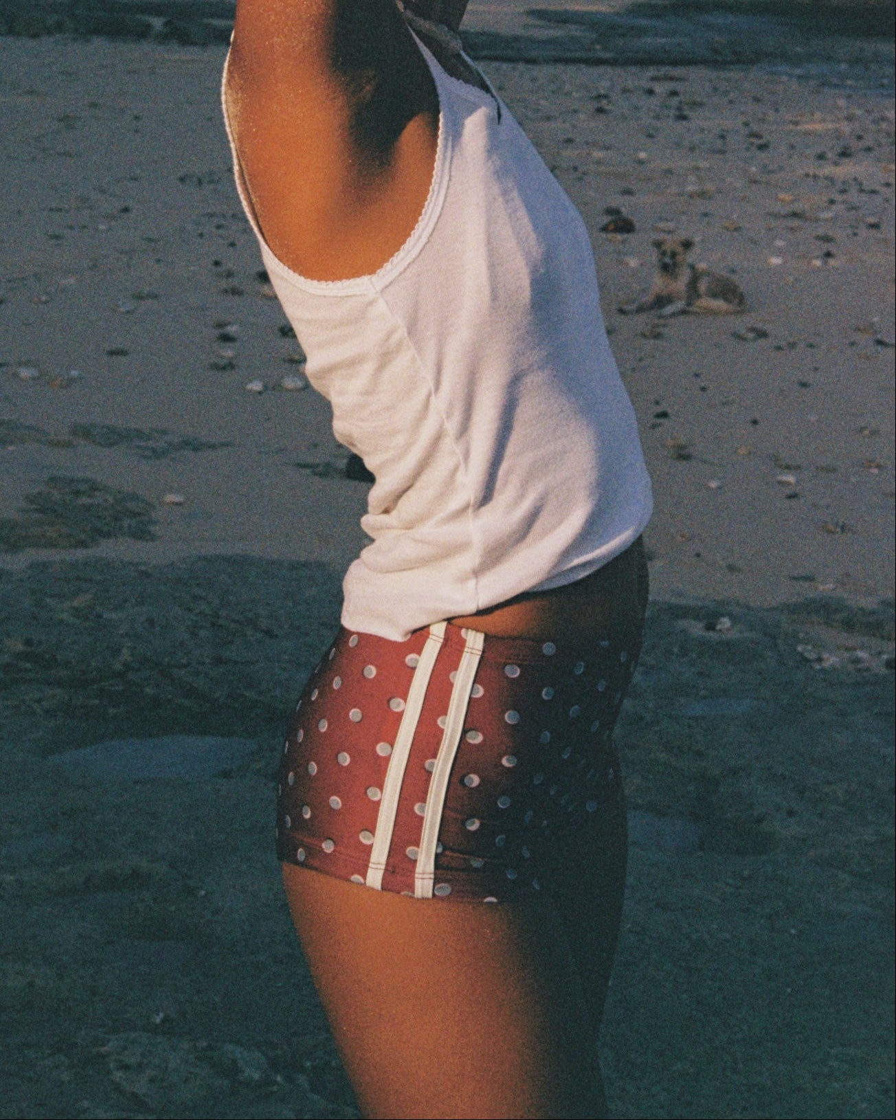 Person wearing a white tank top and polka dot maroon shorts on a beach