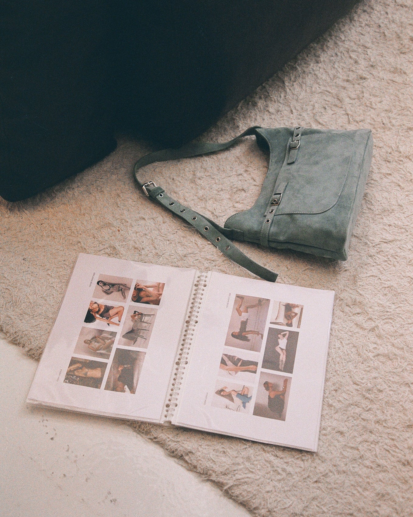 Open photo album with images on a carpeted floor next to a blue suede bag.