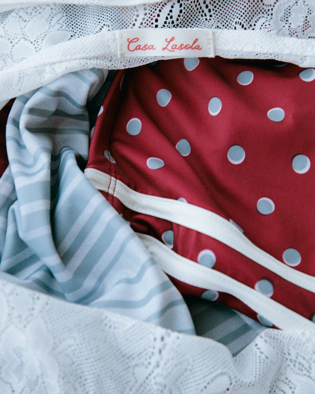 Red and blue polka dot swim inside a white lace bag, with the label 'Casa Lasola' stitched inside.