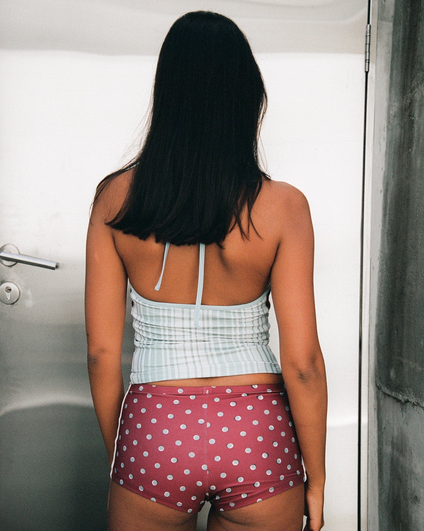 Woman wearing a light blue stripe top and maroon polka dot shorts standing in front of a silver door. 