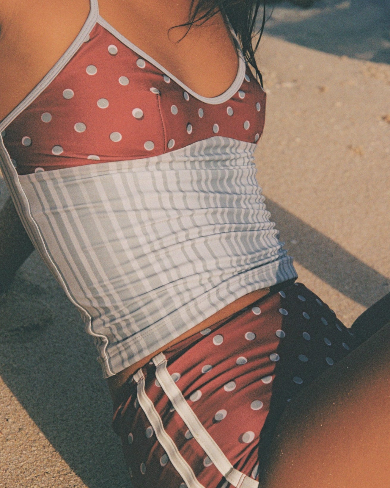 Person wearing a polka dot top and short sitting on a sandy surface.