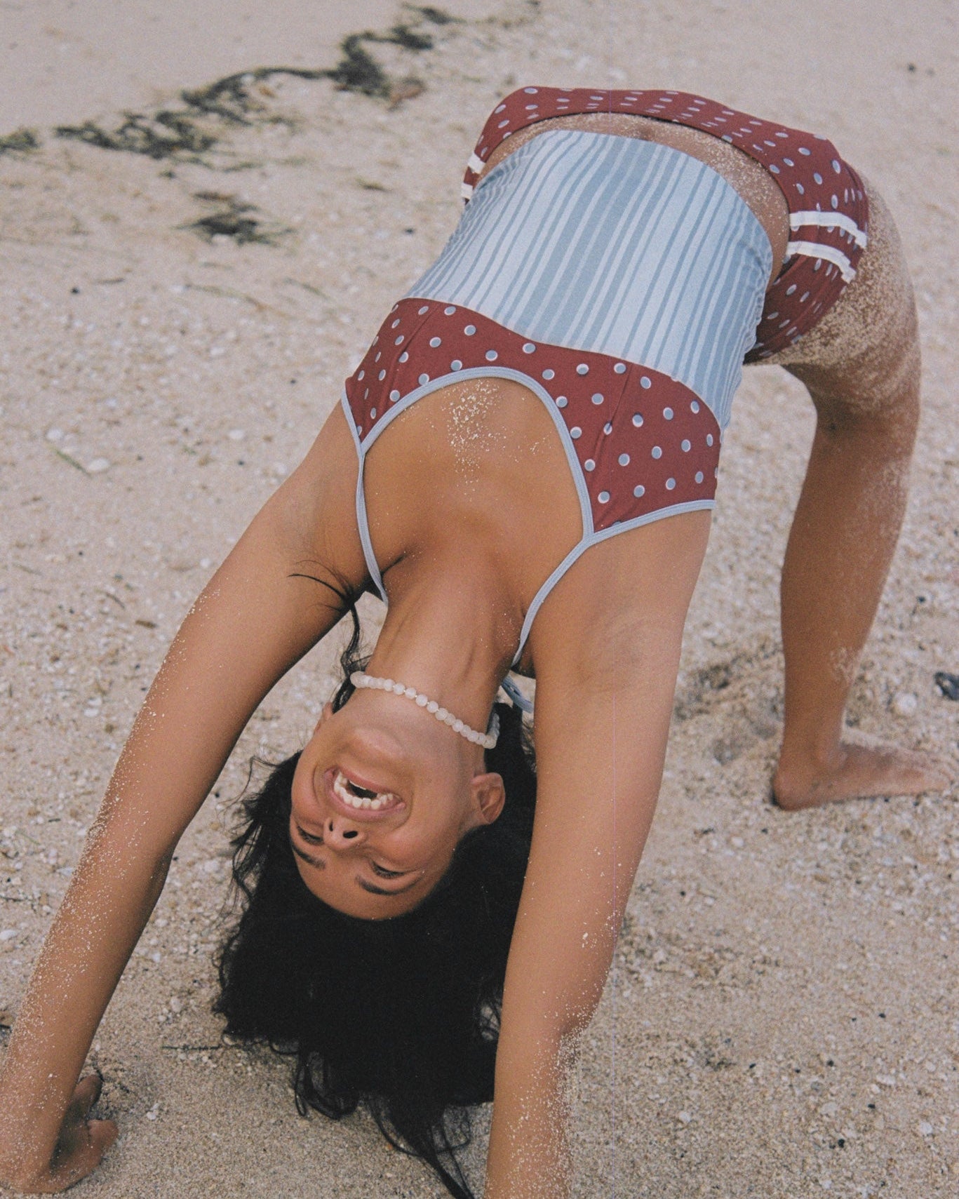 Person in a polka and stripe swimsuit doing a bend back on a sandy beach
