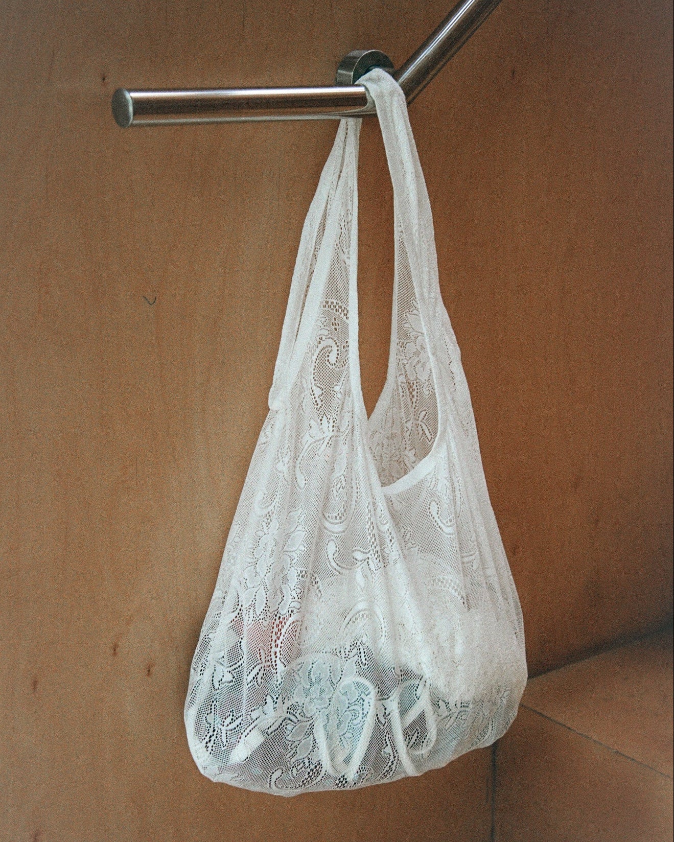 White lace bag hanging on a metal rod against a wooden wall.
