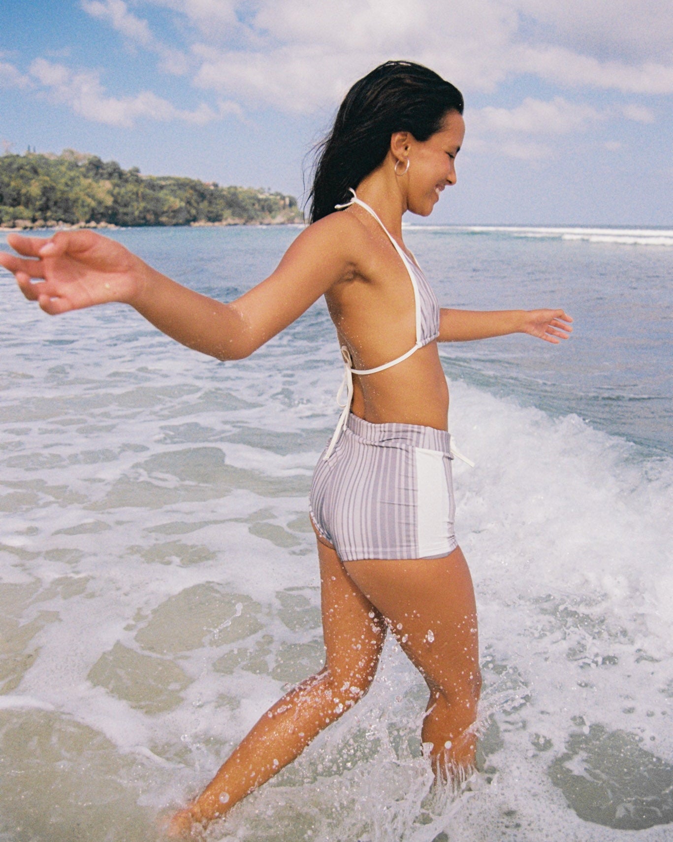Woman in a grey striped bikini standing in shallow water with a scenic background