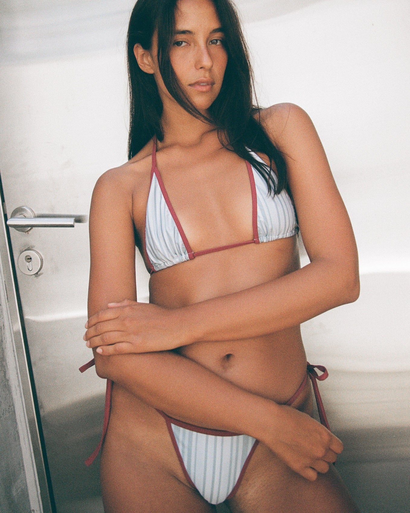 Woman wearing a maroon and blue striped bikini in front of a silver door.
