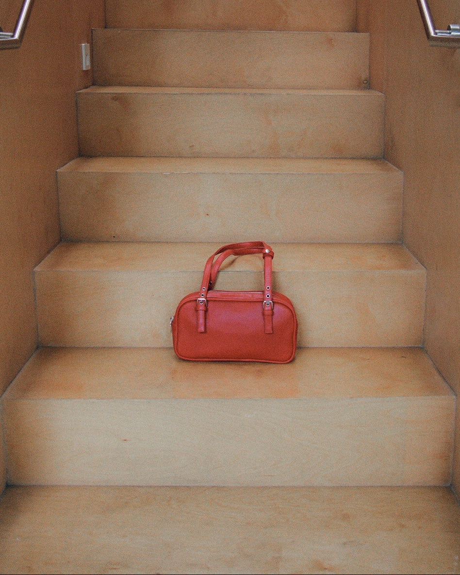 Red leather handbag on a set of beige stairs with metal railings.