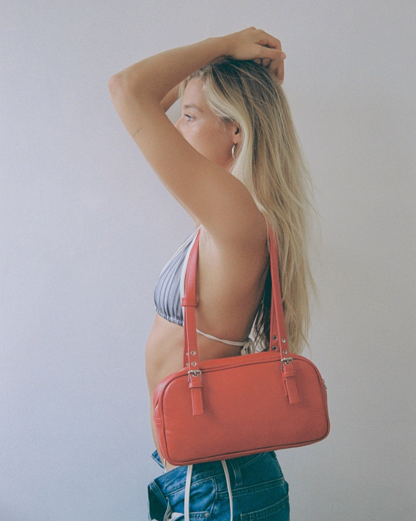 Woman holding a red leather handbag against a plain background