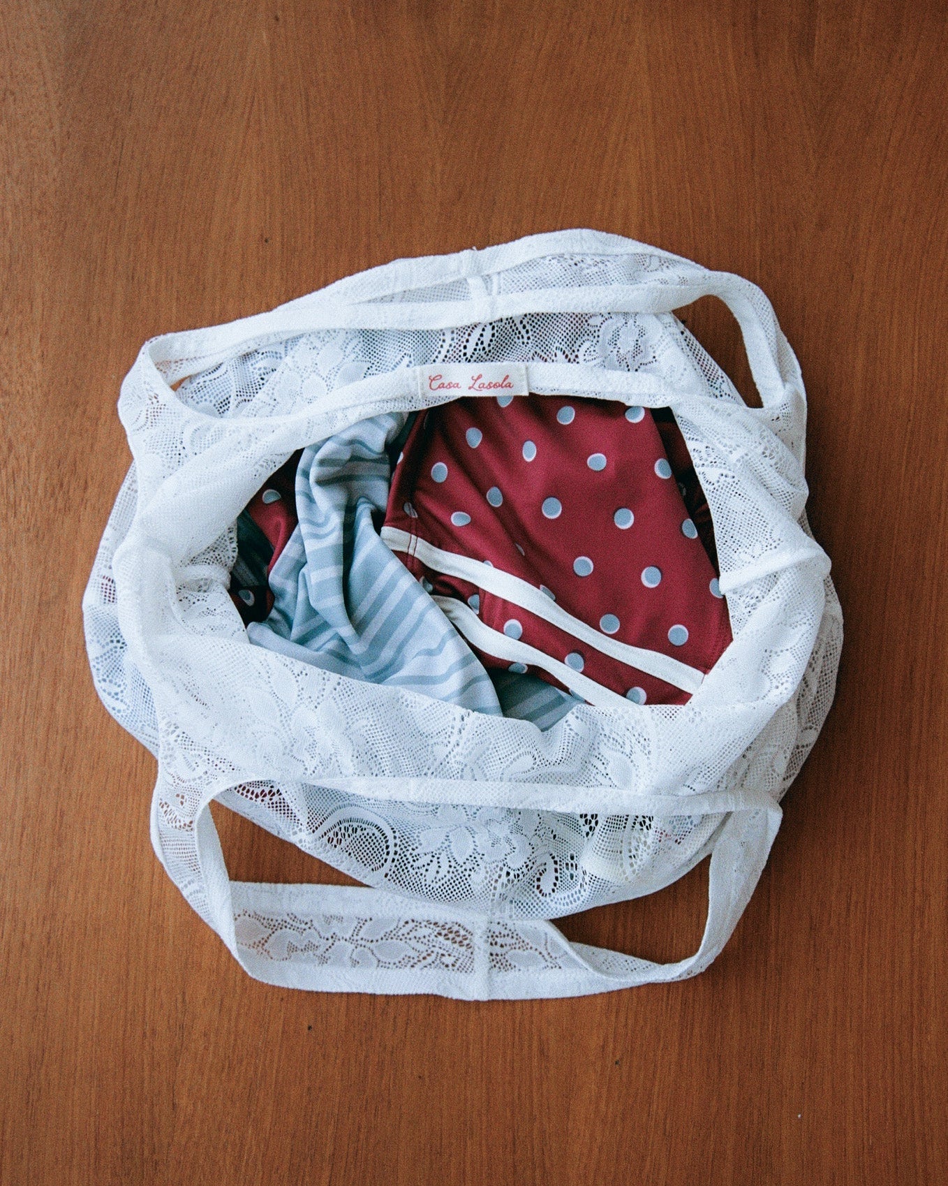 White lace bag filled with swimwear on a wooden surface